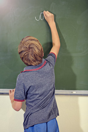 Hes getting the hang of this. A little boy writing on the blackboard during a school lesson.の写真素材