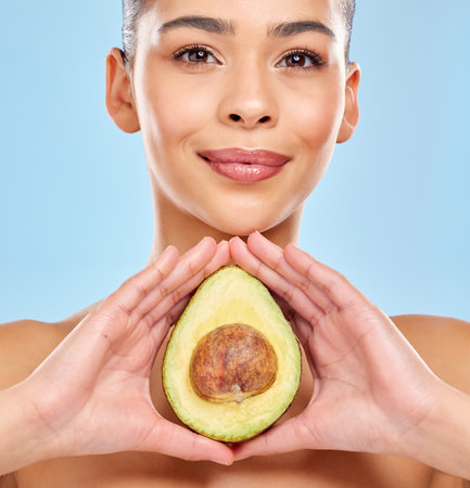 Avocados help in intensely moisturising and conditioning your skin. Studio portrait of an attractive young woman posing with an avocado against a blue background.の写真素材