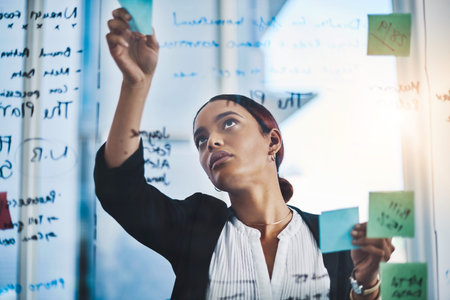 The goal just keeps getting bigger. a young businesswoman brainstorming notes on a glass wall in an...