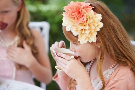 Taking a sip of tea. Two young girls having a tea party in the backyard.の写真素材