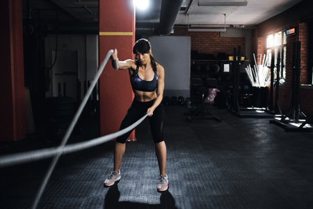 Body under construction. a young woman doing heavy rope training at the gym.の写真素材