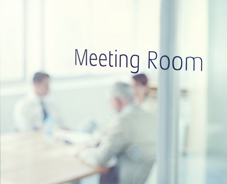 The meeting is in session. Closeup of a glass door reading meeting room with business people blurred in the room behind.の写真素材