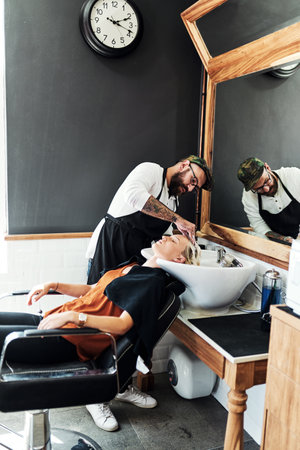 A good wash can do wonders for your hair. an attractive young woman getting her hair washed and styled by a hairdresser inside a salon.の写真素材