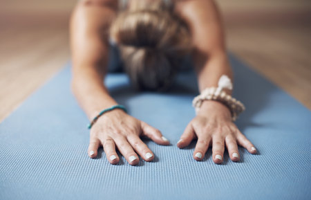 Stretching out the upper back. an unrecognizable woman holding a childs pose during an indoor yoga session alone.の写真素材
