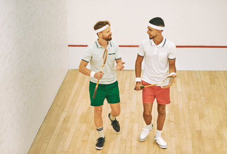 Face your rival with confidence. two young men chatting while playing a game of squash at an indoor court.の写真素材