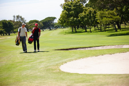 What an awesome day for a game of golf. two men carrying their golf bags across a golf course.の写真素材