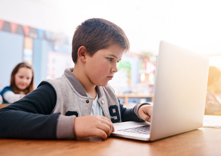 He is full on focussed. a focussed young elementary school kid browsing on a laptop inside of the class during the day.の写真素材