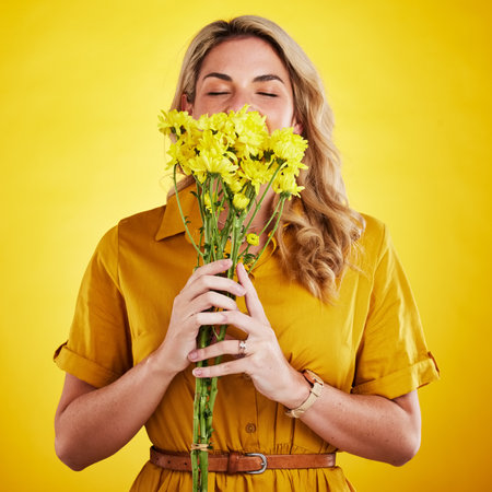 Portrait, smelling and woman with flowers in studio isolated on a yellow background. Floral, bouquet and person sniff, aroma or scent with female model holding natural plants and fresh flower.の写真素材