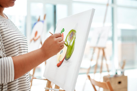 Paying attention to the details. an unrecognizable artist standing and painting on a canvas during a...