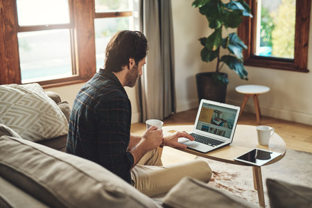 Let the blogging begin. a handsome young man using his laptop while relaxing on a couch at home.の写真素材