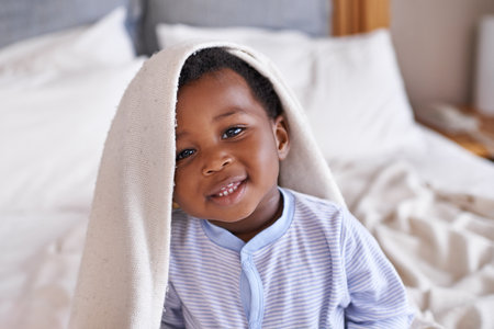 Portrait, happy and baby with a blanket in bed, waking up and playing in his home. Face, smile and african boy toddler in a bedroom curious, having fun and sweet, cute and playful while relaxingの写真素材