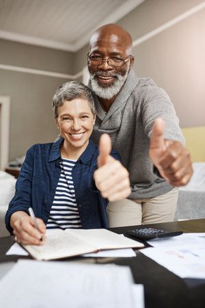 Thumbs up, portrait and senior couple planning, asset management and financial success, winning or thank you. Happy face, finance or interracial people, woman or partner like, yes or ok hands at homeの写真素材