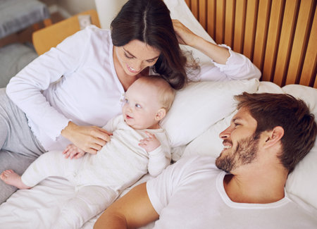 Top view of mom, dad and baby on bed for love, care and quality time together at home. Happy parents, family and newborn kid relax in bedroom with support, childhood development and smile for bondingの写真素材