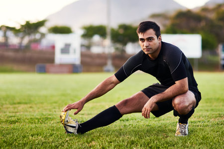 Getting in a warm up before I play. Full length shot of a handsome young sportsman stretching alone before a rugby practice during the day.の写真素材