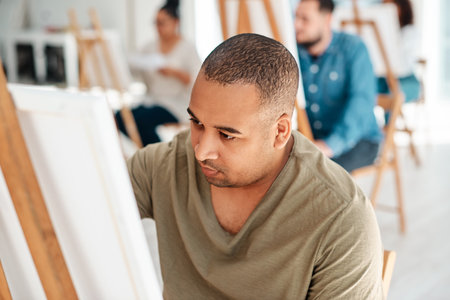 Concentrating on my artwork. a handsome young artist sitting and painting during an art class in the studio.の写真素材