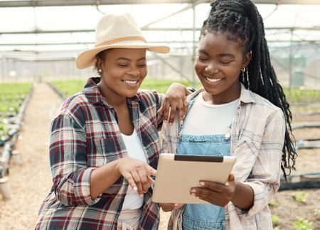 Happy farmers standing in a greenhouse. Two farmers using a digital tablet in the garden. Smiling colleagues collaborating in the plant garden. Coworkers cultivating fresh plant crops.の写真素材