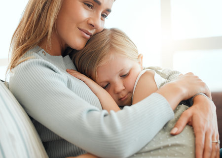 I feel more at home in Mums arms. an adorable little girl cuddled up to her mother during a day at home.の写真素材