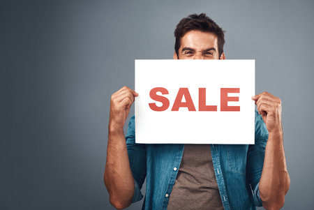 Man, sale and billboard poster for advertising, marketing or branding against a grey studio background. Male person or realtor holding board or sign for sales announcement, notice or advertisementの写真素材
