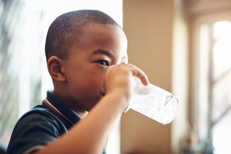 H2O is essential to your childs health. a young boy drinking a glass of water at home.の写真素材