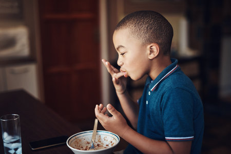 My moms spaghetti is finger licking good. a young boy eating a bowl of spaghetti at home.の写真素材