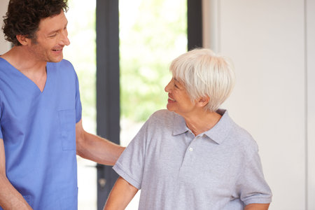 Friendly support for recovering patients. a male nurse checking on a senior patient.