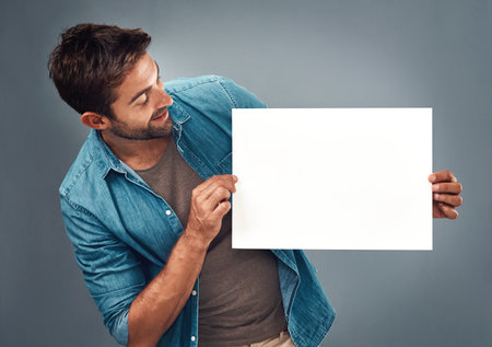 Man, billboard sign and mockup for marketing, advertising or branding against a grey studio background. Male person holding rectangle shape poster or placard for advertisement message with copy spaceの写真素材