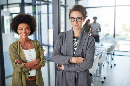 Were a team built for success. Portrait of young creatives standing in a modern office with colleagues in the background.の写真素材