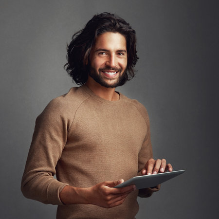 I keep my lifestyle digitized. Studio shot of a handsome young man using a digital tablet against a gray background.の写真素材