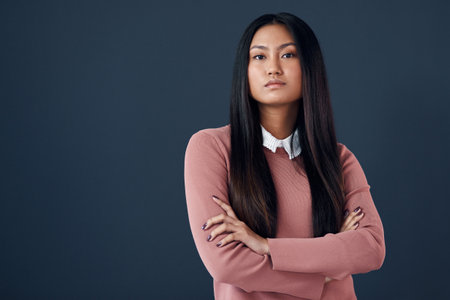 Confident, portrait of Korean woman and in a studio background with her arms crossed. Empowerment or elegant, corporate worker and pose with serious or proud young businesswoman in a backdrop.の写真素材