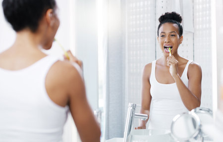 Woman brushing teeth in bathroom, mirror and oral hygiene, morning routine with toothbrush and dental health. Female person at home, grooming and self care, clean mouth with toothpaste and wellnessの写真素材