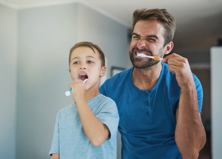 Happy, brushing teeth and father with son in bathroom for morning routine, bonding and dental. Oral hygiene, cleaning and smile with man and child in mirror of family home for self care and wellnessの写真素材