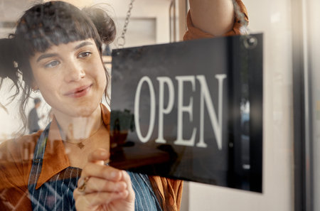 Ready to make some customers smile. a young business owner hanging up an open for business sign.