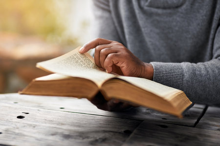 Hands, story and a man reading the bible at a table outdoor in the park for faith or belief in god. Book, religion and spiritual with a male christian sitting in the garden for learning or worshipの写真素材