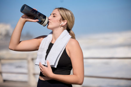 Fitness, music and woman drinking water at the beach for sports, running and cardio routine....