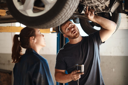 Working together to decide the best course of action. two mechanics working under a car in an auto repair shop.の写真素材