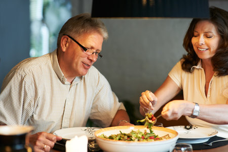Dig in. a senior couple sharing a romantic meal at home.の写真素材