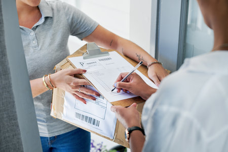 Sign here, please. an unrecognizable woman standing and signing for her package from the courier.の写真素材