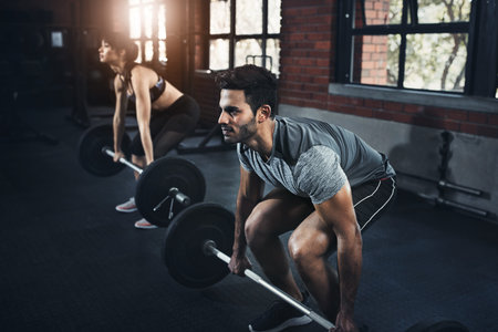 Targeting the major muscle groups. a young man and woman working out with weights at the gym.