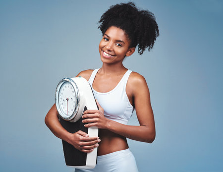 The scale is my best friend. Studio shot of an attractive young woman holding a weight scale.の写真素材