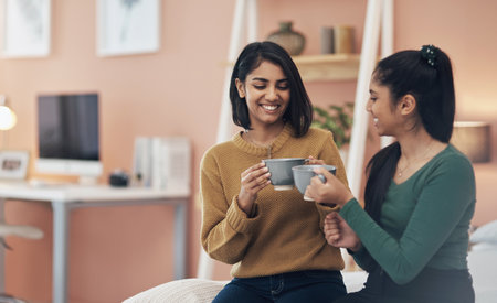 Having a sister means you have a best friend for a lifetime. two young women drinking coffee while sitting together at home.の写真素材