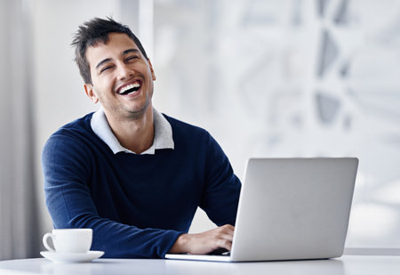 My career is trending. Portrait of a smiling young businessman using a laptop while sitting at a desk in an office.の写真素材