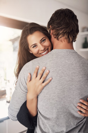 Portrait of happy woman, man and hug of love, care and quality time together for commitment to relationship at home. Young couple, smile and hugging for romance, trust and relax with partner in houseの写真素材