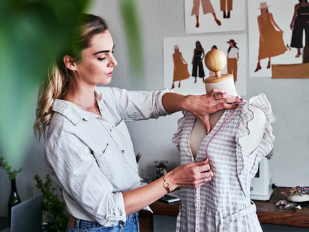 Fashion, sustainable business and woman designer with mannequin, measuring tape and creative startup. Focus, creativity and tailor with dress on doll, eco friendly design on clothes in textile studioの写真素材