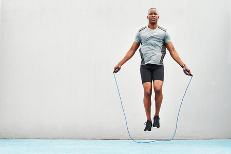Jump, rope and training with black man skipping in stadium for sports, workout practice and cardio. Health and body with athlete jumping on track for strong, mockup space and exercise against wallの写真素材