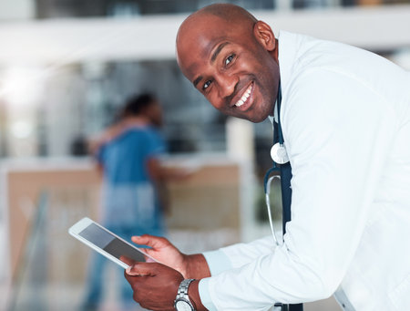 His day is going rather well today. Portrait of a cheerful young doctor browsing on a digital tablet while standing in a hospital during the day.の写真素材