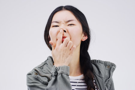 Portrait, funny face and nose with an asian woman in studio on gray background looking silly or goofy. Comedy, comic and crazy with a happy young female person joking indoor for playful fun or humorの写真素材