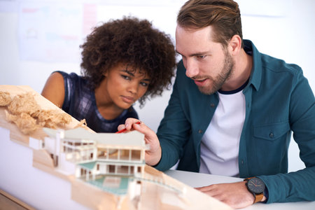 Hes a perfectionist. two young architects working on a model of a building.の写真素材