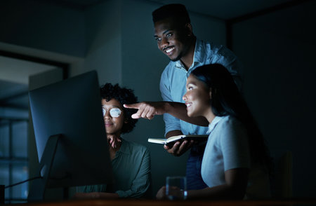 When you eat, sleep and breathe the brand. a group of young businesspeople using a computer together during a late night at work.の写真素材