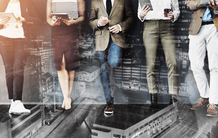 Getting their feet into the door of business. Cropped studio shot of a group of businesspeople using wireless technology while waiting in line against a gray background.の写真素材