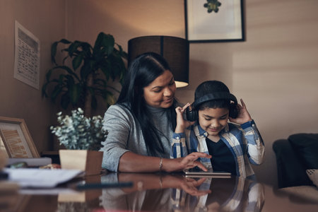 Nothing reminded us of the importance of parenting like quarantine. an adorable little boy using a digital tablet and headphones while completing a school assignment with his mother at home.の写真素材